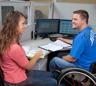 180 Medical employee sitting at a desk with another employee in a wheelchair